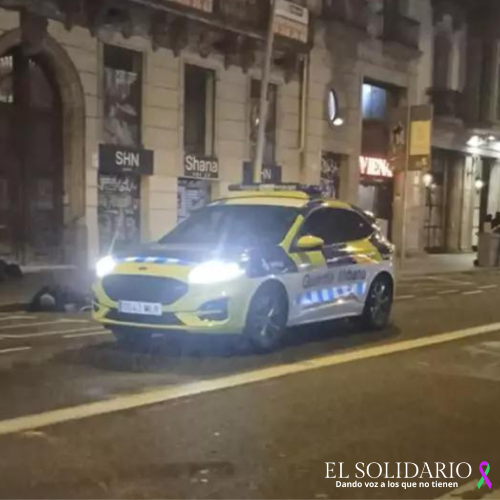 Un coche patrulla pasa por delante de un hombre tendido en la calle Pelai