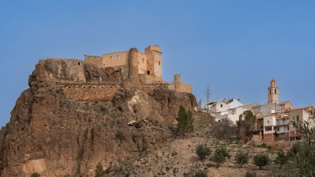 A scenic view of Cofrentes Castle perched on a rocky hill in Comunidad Valenciana, Spain.