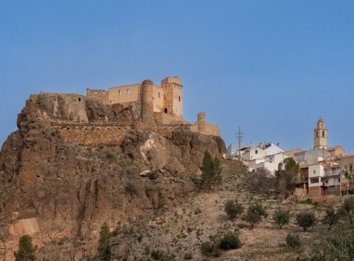 A scenic view of Cofrentes Castle perched on a rocky hill in Comunidad Valenciana, Spain.