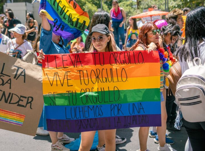 Colorful LGBTQ pride parade with participants holding rainbow flags and signs advocating equality.