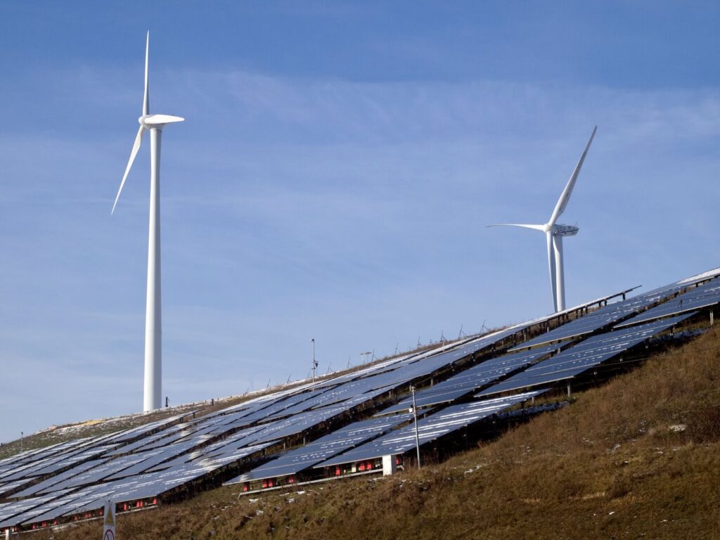Wind turbines and solar panels on a hillside harnessing renewable energy under a clear sky.