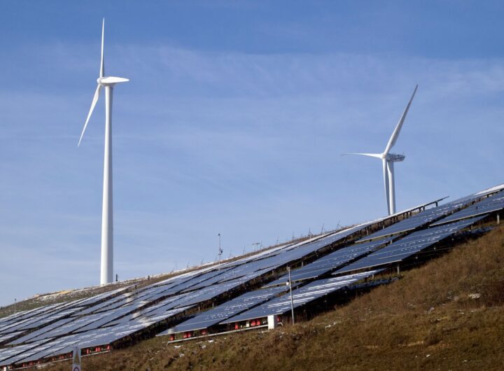 Wind turbines and solar panels on a hillside harnessing renewable energy under a clear sky.