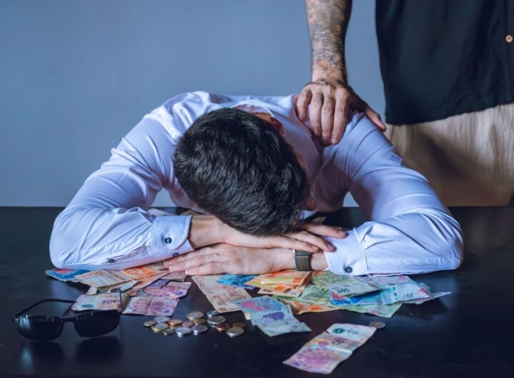 Depressed man surrounded by Argentine pesos represents financial stress and burnout.