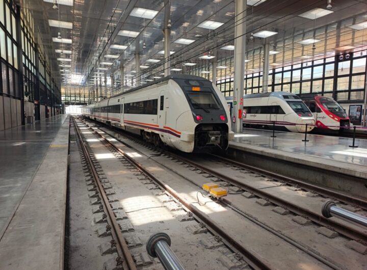 Interior view of a modern railway station in Cádiz, featuring multiple trains on parallel tracks.