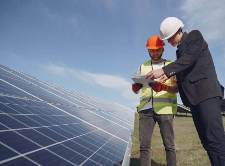 Low angle of young inspector and foreman in hardhats checking documentation against modern solar panels in field