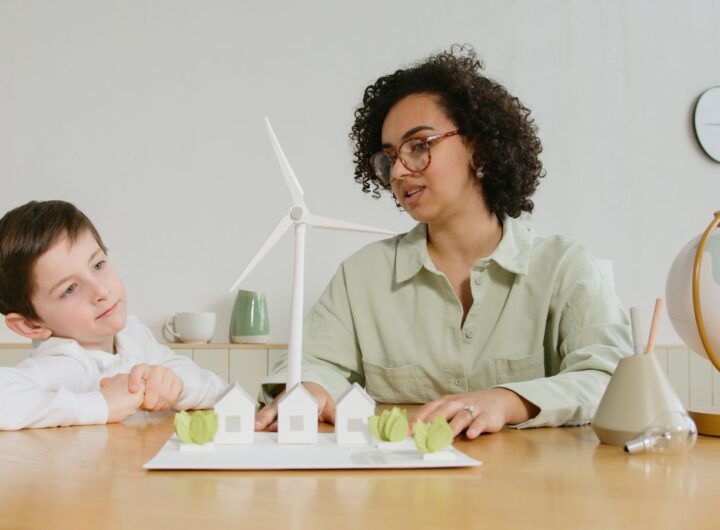 A child and teacher explore renewable energy concepts with a wind turbine model indoors.