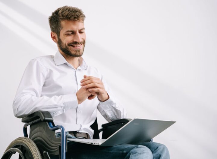 Confident man in a wheelchair working on a laptop indoors with a smile.