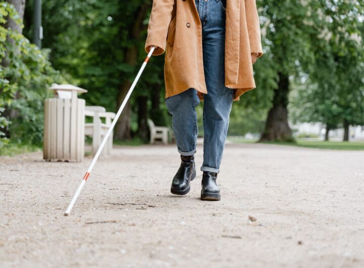 A visually impaired person using a white cane walks through a green park.