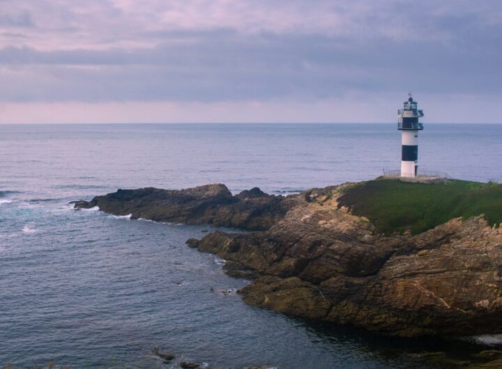 white and brown lighthouse on brown rock formation beside sea during daytime