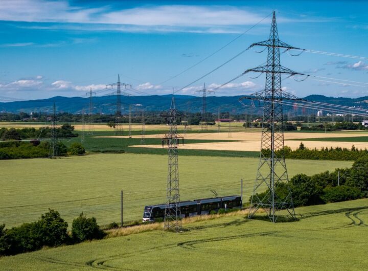 Train travels through green fields with power lines.