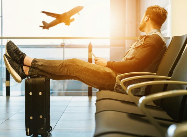 man sitting on gang chair with feet on luggage looking at airplane