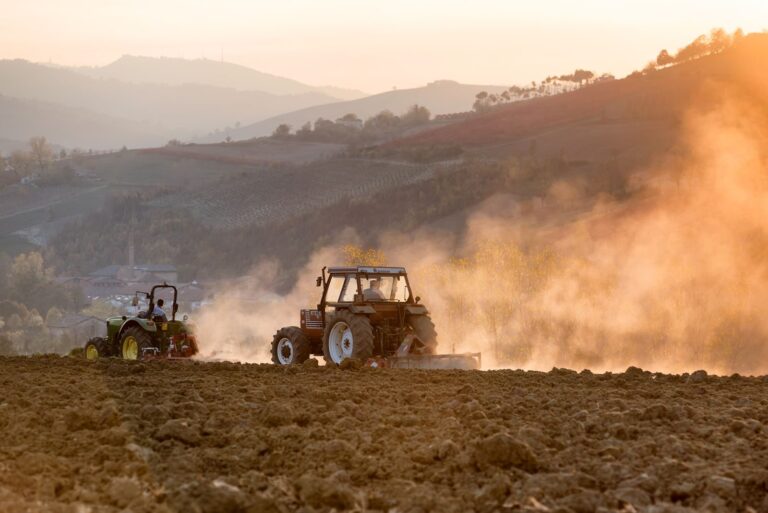 A tractor plowing a field at sunset in the rolling hills of Castelvetro di Modena, Italy.