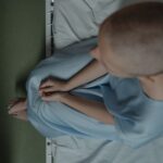 Bald patient sitting on hospital bed, expressing vulnerability and introspection.