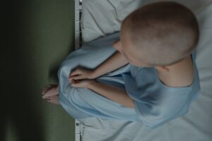 Bald patient sitting on hospital bed, expressing vulnerability and introspection.