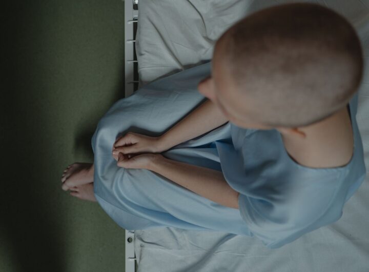 Bald patient sitting on hospital bed, expressing vulnerability and introspection.