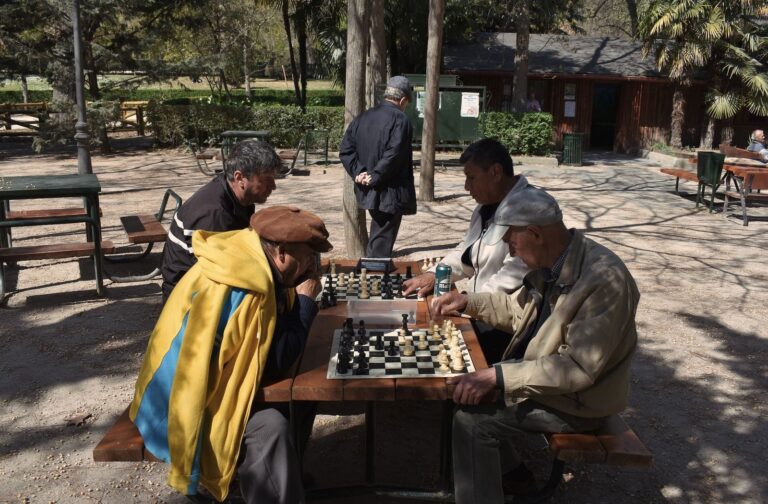 Senior men enjoying a chess game outdoors in a sunny Madrid park setting.